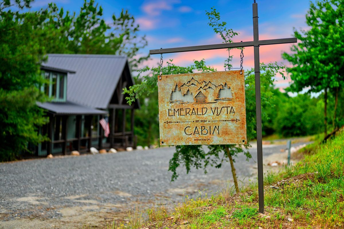 The Emerald Vista Cabin sign hanging at the driveway, cabin behind it at dusk